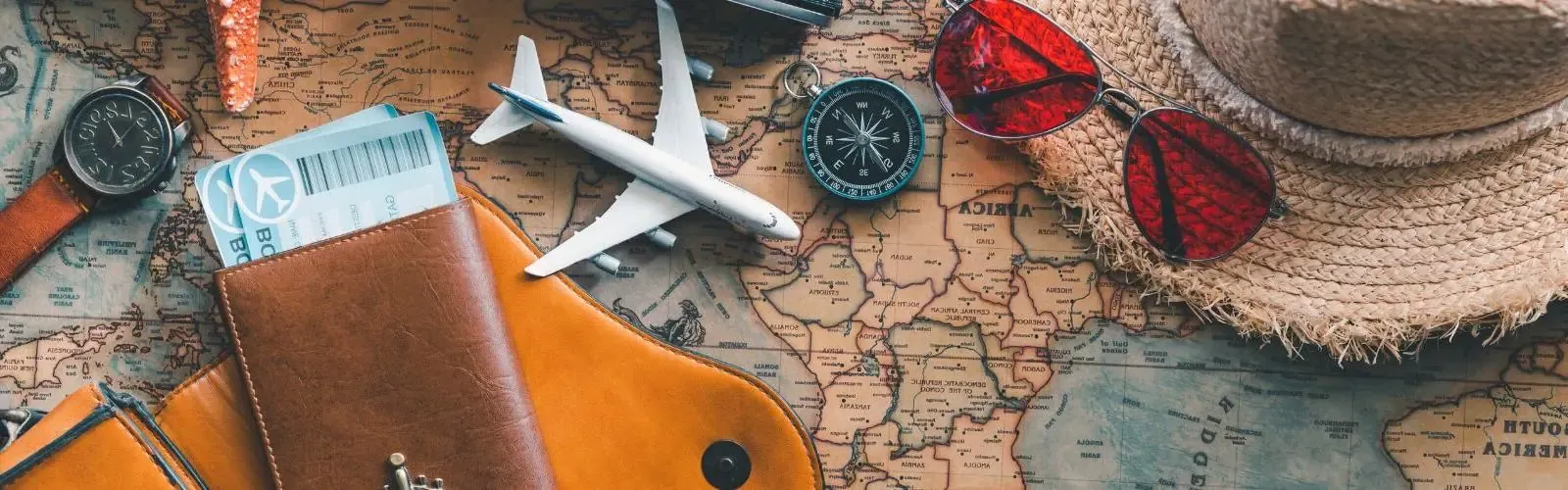 Map with travel trinkets on top of it like a hat, sunglasses and miniature plane.